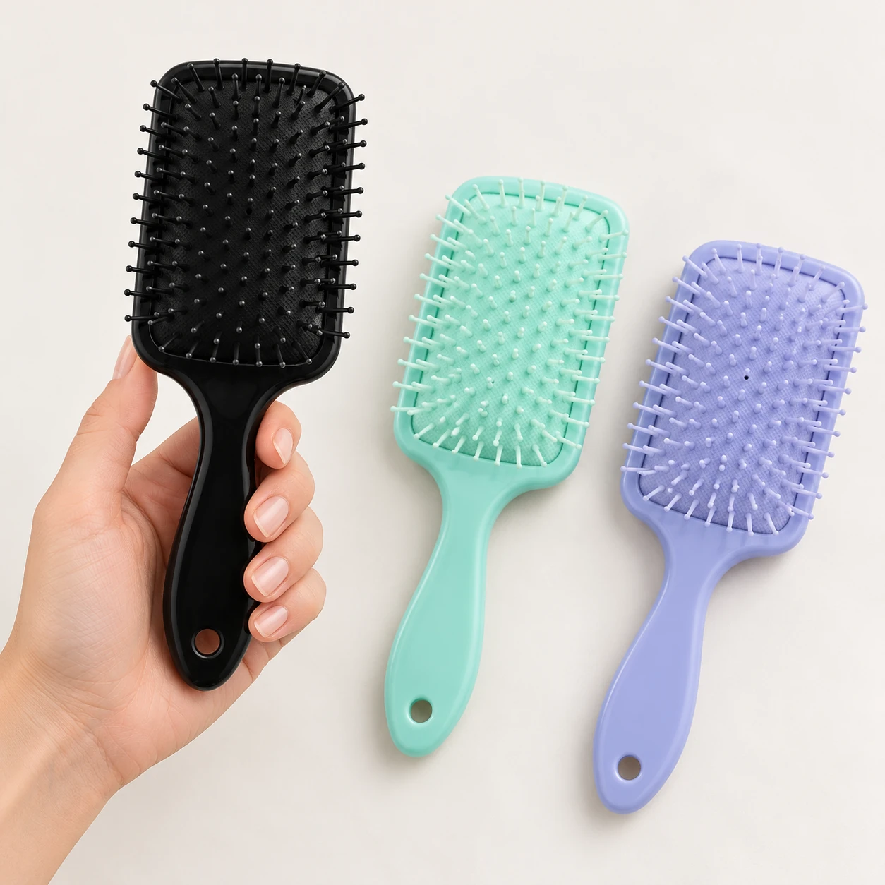 Zwarte Elina Hair haarborstel in een hand, met de mintgroene en lila variant ernaast